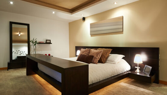 Image is of a beautiful modern bedroom with lighting under the bed as well as on the ceiling.