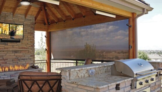 Outdoor grilling and seating area with a wall-mounted TV display and Insolroll solar shades partially lowered.