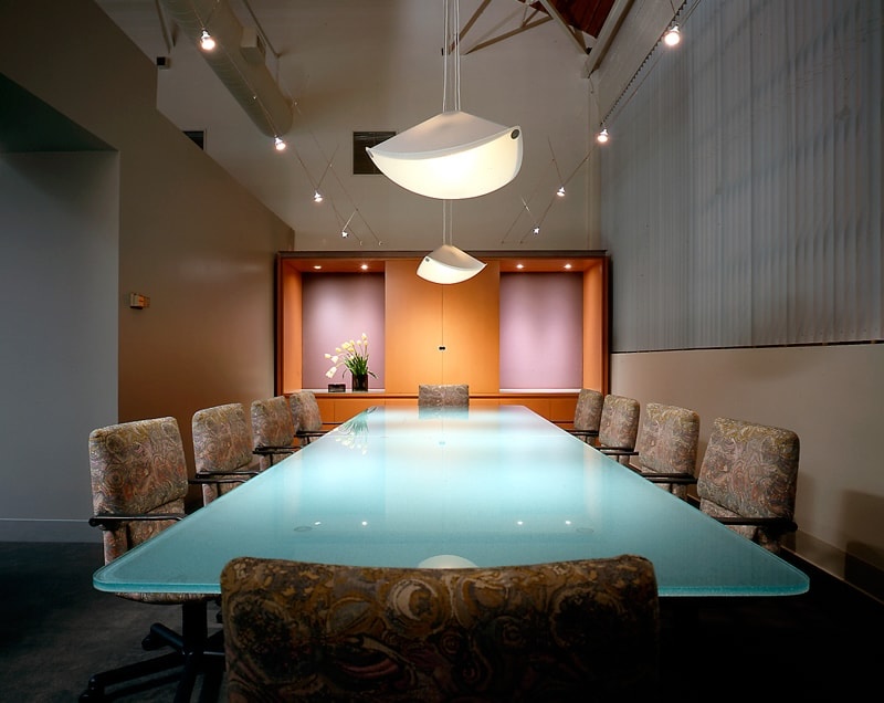 A glass top conference table with chairs surrounding it. Modern pendant lighting hangs above the table.