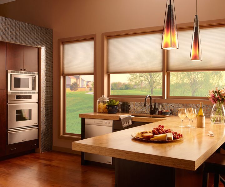 A beautifully illuminated kitchen with soft pendant lights and automated shades partially lowered.