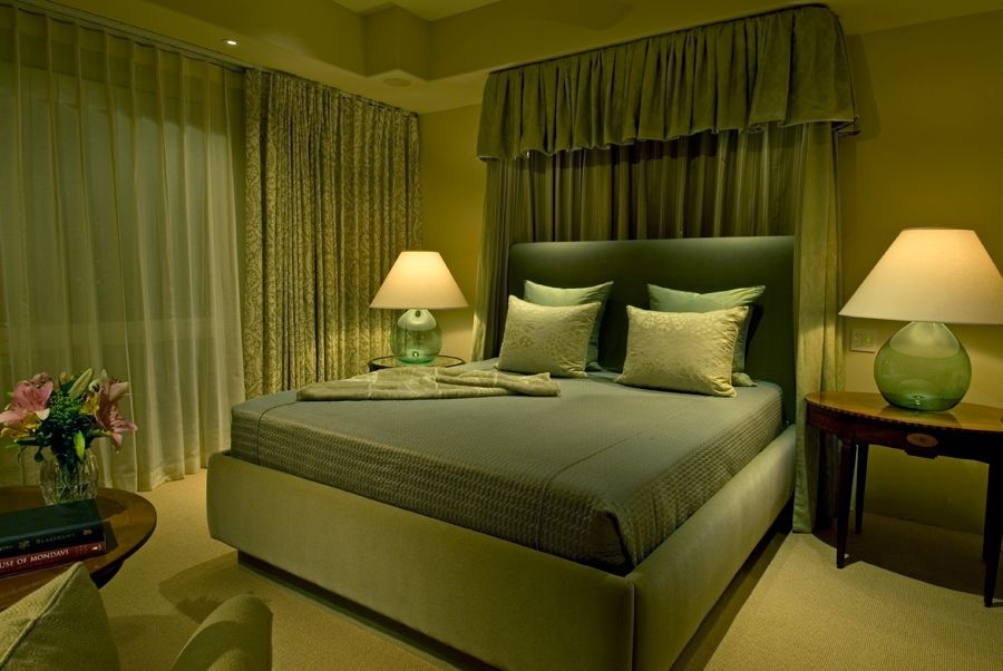 Elegant bedroom with soft green tones, Lutron-controlled lighting, sheer curtains, and ambient bedside lamps at dusk.