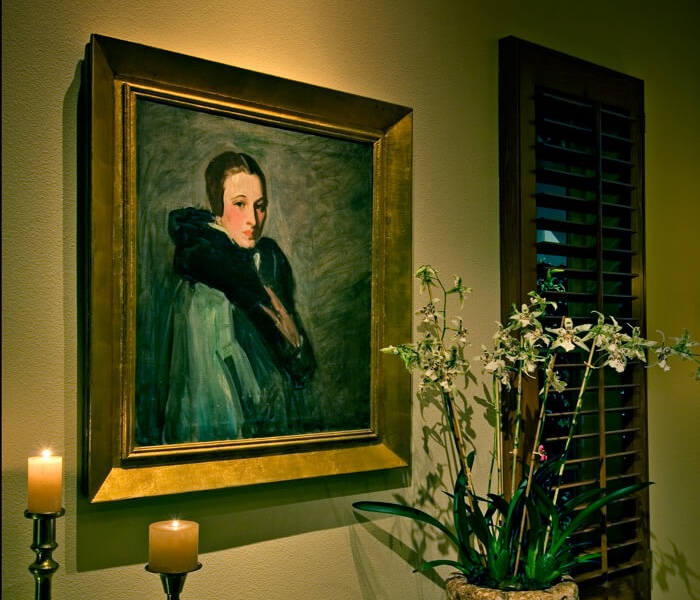 Framed portrait lighting highlights a classic painting above orchids and candles, creating a warm, elegant vignette.