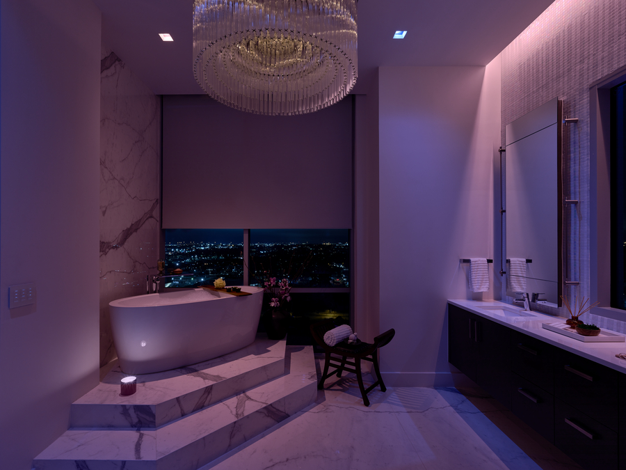 Lutron motorized roller shades partially lowered in a high-end bathroom with steps leading to tub.