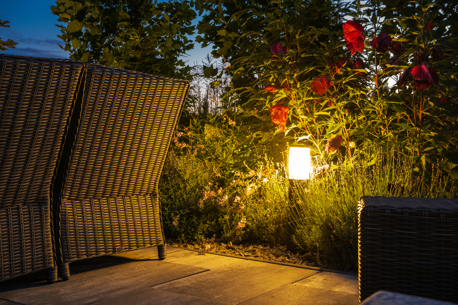 In-ground lighting fixture in an outdoor patio area. A patio chair and foliage surround the wayfinding light.